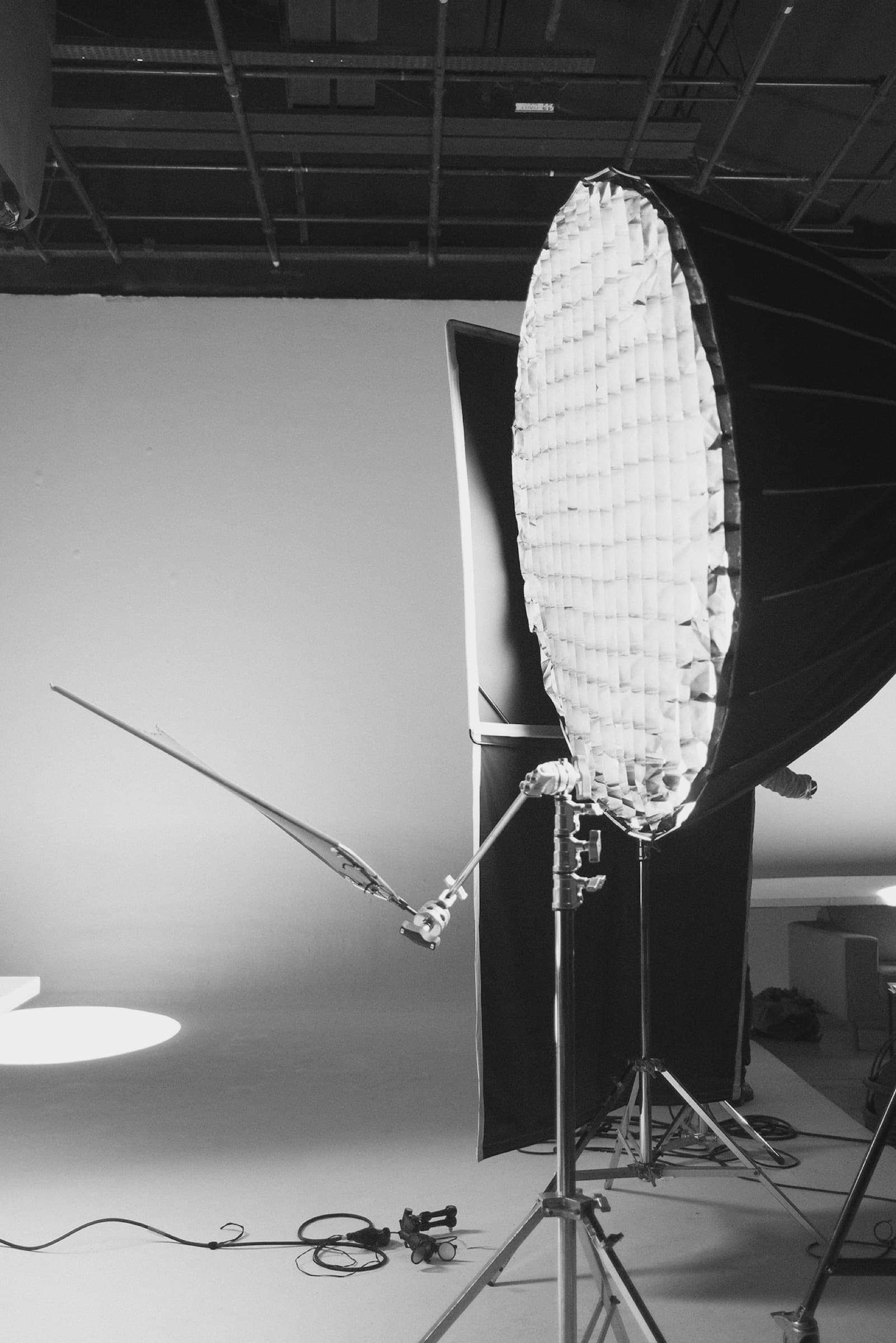A large gridded softbox and a boom arm on stands under the studio rigging