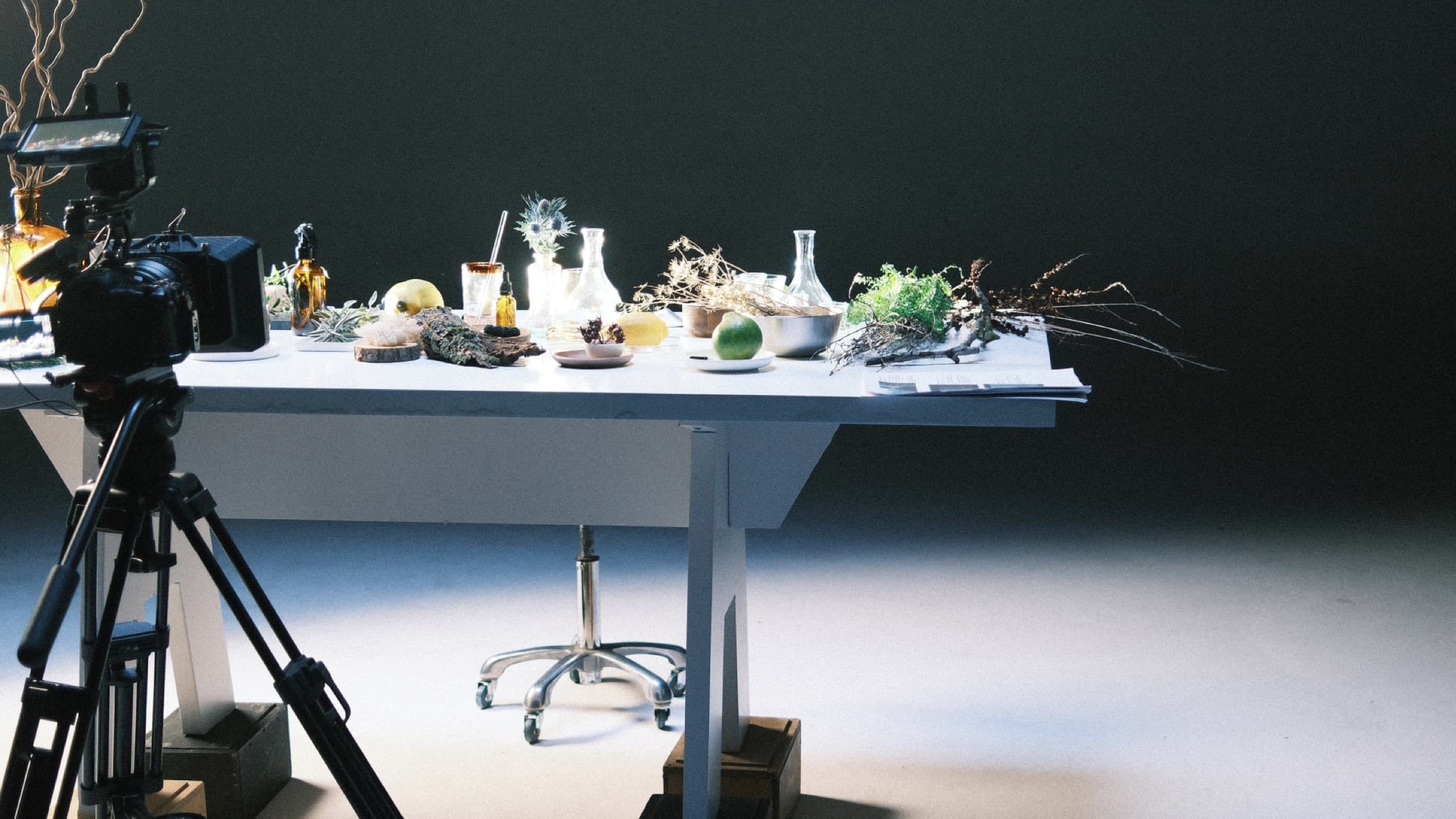 A long white table laid with botanicals, citrus, glassware and small bottles in a film studio